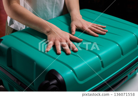 Traveler opening luggage, Close shot of hands unfastening suitcase zipper before travel, Detailed view of hands pulling zipper on vibrant teal travel case with anticipation Traveler opening luggage, Close shot of hands unfastening suitcase zipper before travel, Detailed view of hands pulling zipper on vibrant teal travel case with anticipation 136071558