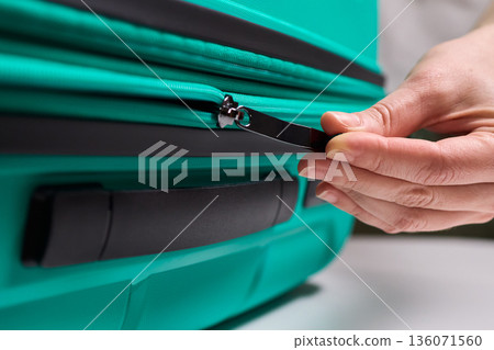 Traveler opening luggage, Close shot of hands unfastening suitcase zipper before travel, Detailed view of hands pulling zipper on vibrant teal travel case with anticipation Traveler opening luggage, Close shot of hands unfastening suitcase zipper before travel, Detailed view of hands pulling zipper on vibrant teal travel case with anticipation 136071560