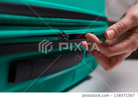 Traveler opening luggage, Close shot of hands unfastening suitcase zipper before travel, Detailed view of hands pulling zipper on vibrant teal travel case with anticipation Traveler opening luggage, Close shot of hands unfastening suitcase zipper before travel, Detailed view of hands pulling zipper on vibrant teal travel case with anticipation 136071567