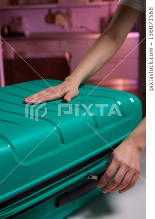 Traveler opening luggage, Close shot of hands unfastening suitcase zipper before travel, Detailed view of hands pulling zipper on vibrant teal travel case with anticipation Traveler opening luggage, Close shot of hands unfastening suitcase zipper before travel, Detailed view of hands pulling zipper on vibrant teal travel case with anticipation 136071568