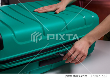 Traveler opening luggage, Close shot of hands unfastening suitcase zipper before travel, Detailed view of hands pulling zipper on vibrant teal travel case with anticipation 136071582