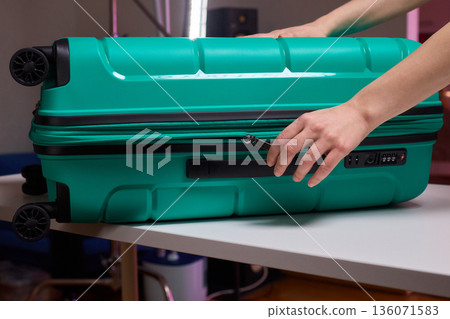 Traveler opening luggage, Close shot of hands unfastening suitcase zipper before travel, Detailed view of hands pulling zipper on vibrant teal travel case with anticipation 136071583