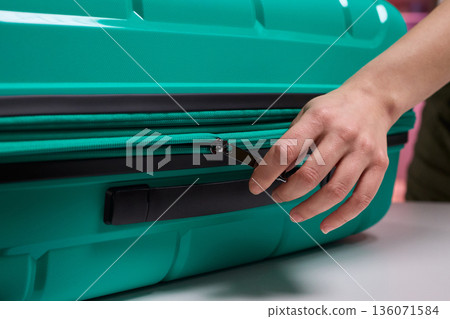 Traveler opening luggage, Close shot of hands unfastening suitcase zipper before travel, Detailed view of hands pulling zipper on vibrant teal travel case with anticipation Traveler opening luggage, Close shot of hands unfastening suitcase zipper before travel, Detailed view of hands pulling zipper on vibrant teal travel case with anticipation 136071584