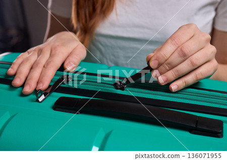 Traveler opening luggage, Close shot of hands unfastening suitcase zipper before travel, Detailed view of hands pulling zipper on vibrant teal travel case with anticipation 136071955