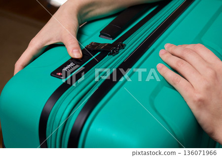 Secure suitcase with combo lock, Hands set combination on teal suitcase with textured surface, Closeup of hands adjusting numeric lock on stylish teal travel suitcase Secure suitcase with combo lock, Hands set combination on teal suitcase with textured surface, Closeup of hands adjusting numeric lock on stylish teal travel suitcase 136071966