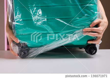 Luggage wrapping process, Worker securing suitcase with protective plastic film, Ensuring safety and protection through meticulous wrapping of belongings for travel Luggage wrapping process, Worker securing suitcase with protective plastic film, Ensuring safety and protection through meticulous wrapping of belongings for travel 136071971