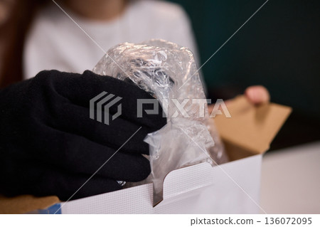 Worker examines package cautiously, Warehouse employee checks sealed box meticulously, Focused employee carefully inspects and cuts tape on parcel in warehouse setting Worker examines package cautiously, Warehouse employee checks sealed box meticulously, Focused employee carefully inspects and cuts tape on parcel in warehouse setting 136072095