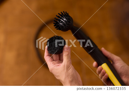 Household brushes examined closely, Two brushes analyzed in indoor setting, Person holding two black brushes inspecting bristle arrangement for household cleaning purposes 136072335