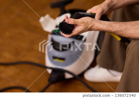 Household brushes examined closely, Two brushes analyzed in indoor setting, Person holding two black brushes inspecting bristle arrangement for household cleaning purposes 136072340