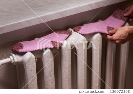 Person placing moist wool socks onto heated radiator fins, Detailed scene of hand carefully positioning damp wool socks on heated metal radiator with knit texture Person placing moist wool socks onto heated radiator fins, Detailed scene of hand carefully positioning damp wool socks on heated metal radiator with knit texture 136072398