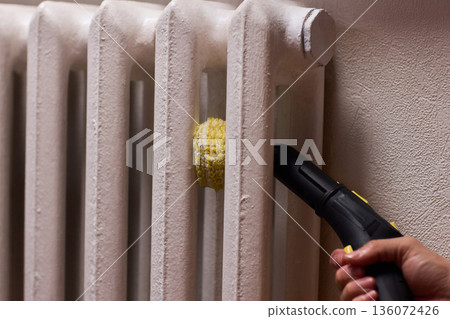 Brass brush during radiator cleaning, Closeup of hand using steam to clean radiator, Careful hand cleaning cast iron radiator with steam and brass brush in home environment Brass brush during radiator cleaning, Closeup of hand using steam to clean radiator, Careful hand cleaning cast iron radiator with steam and brass brush in home environment 136072426