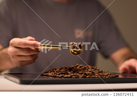 Detail oriented scene of coffee professional measuring beans carefully, An intimate scene depicting barista accurately measuring roasted coffee beans with gold scoop 136072431