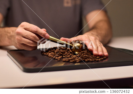 Detail oriented scene of coffee professional measuring beans carefully, An intimate scene depicting barista accurately measuring roasted coffee beans with gold scoop Detail oriented scene of coffee professional measuring beans carefully, An intimate scene depicting barista accurately measuring roasted coffee beans with gold scoop 136072432