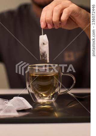 Pouring green tea into clear glass cup, Closeup of peaceful tea brewing scene at dawn, An intimate moment of preparing green tea with gentle lighting and scattered leaves Pouring green tea into clear glass cup, Closeup of peaceful tea brewing scene at dawn, An intimate moment of preparing green tea with gentle lighting and scattered leaves 136072446
