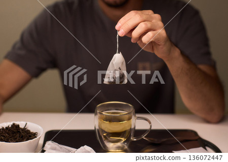 Pouring green tea into clear glass cup, Closeup of peaceful tea brewing scene at dawn, An intimate moment of preparing green tea with gentle lighting and scattered leaves Pouring green tea into clear glass cup, Closeup of peaceful tea brewing scene at dawn, An intimate moment of preparing green tea with gentle lighting and scattered leaves 136072447