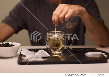 Pouring green tea into clear glass cup, Closeup of peaceful tea brewing scene at dawn, An intimate moment of preparing green tea with gentle lighting and scattered leaves Pouring green tea into clear glass cup, Closeup of peaceful tea brewing scene at dawn, An intimate moment of preparing green tea with gentle lighting and scattered leaves 136072448