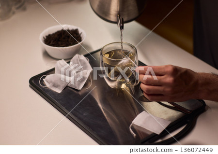 Pouring green tea into clear glass cup, Closeup of peaceful tea brewing scene at dawn, An intimate moment of preparing green tea with gentle lighting and scattered leaves Pouring green tea into clear glass cup, Closeup of peaceful tea brewing scene at dawn, An intimate moment of preparing green tea with gentle lighting and scattered leaves 136072449
