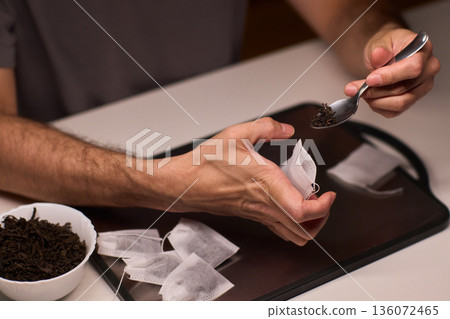 Artisan tea bag filling process, Careful and detailed artisanal approach to tea packaging, Meticulous handpicked tea bags with loose leaves and scattered empty sachets on tray Artisan tea bag filling process, Careful and detailed artisanal approach to tea packaging, Meticulous handpicked tea bags with loose leaves and scattered empty sachets on tray 136072465