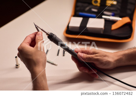 Precision soldering procedure, Hands meticulously align soldering tool precisely, Technician in closeup carefully adjusting soldering tip with safety and measurement focus 136072482