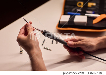 Precision soldering procedure, Hands meticulously align soldering tool precisely, Technician in closeup carefully adjusting soldering tip with safety and measurement focus 136072483