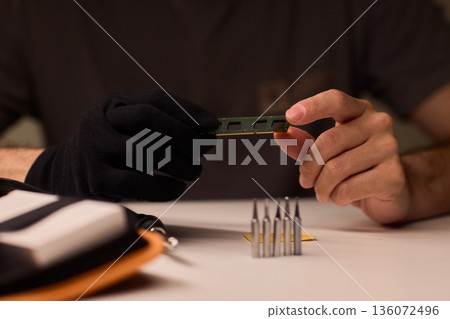 Individual carefully inspecting SODIMM memory module in detailed review, Technician performing detailed visual assessment of RAM stick with neutral lighting and focused attention 136072496