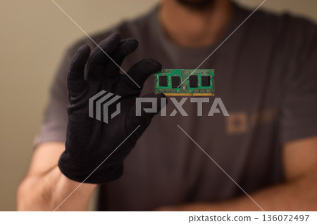 Individual carefully inspecting SODIMM memory module in detailed review, Technician performing detailed visual assessment of RAM stick with neutral lighting and focused attention 136072497