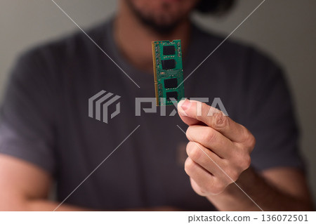 Individual carefully inspecting SODIMM memory module in detailed review, Technician performing detailed visual assessment of RAM stick with neutral lighting and focused attention 136072501