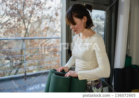Woman organizing yoga mats in studio before practice Woman organizing yoga mats in studio before practice 136072605