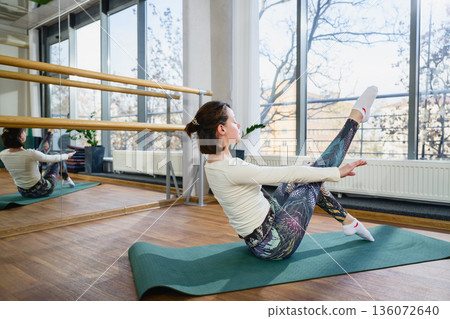 Woman practicing boat pose yoga exercise with mirror reflection in studio Woman practicing boat pose yoga exercise with mirror reflection in studio 136072640