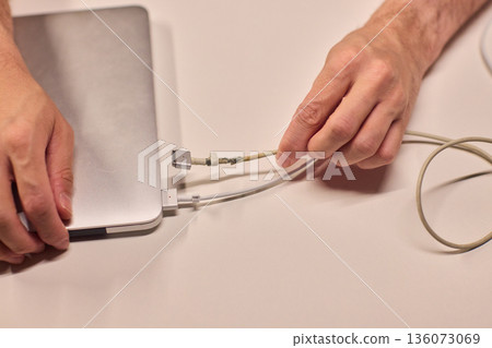 Repairing laptop power cord, Detailed image of fixing broken laptop charger wire, Closeup of skillful person restoring worn electrical cord for portable computer 136073069