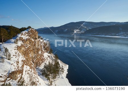 Yenisei river flowing past a snow-covered cliff and distant mountains, Karaulnenskoye Highlands winter landscape. Travel to Siberia. Yenisei river flowing past a snow-covered cliff and distant mountains, Karaulnenskoye Highlands winter landscape. Travel to Siberia. 136073190