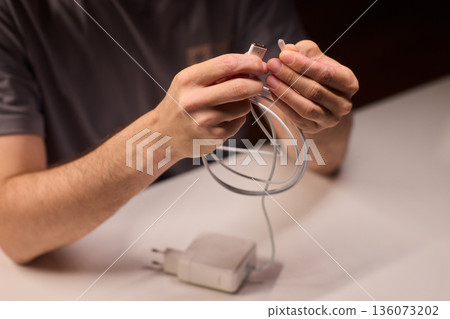 Technician examining charger carefully, Closeup of hands inspecting laptop cable, Meticulous technician performing detailed inspection of laptop power supply before packaging Technician examining charger carefully, Closeup of hands inspecting laptop cable, Meticulous technician performing detailed inspection of laptop power supply before packaging 136073202