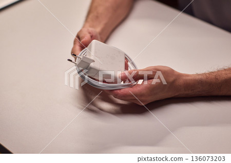 Technician examining charger carefully, Closeup of hands inspecting laptop cable, Meticulous technician performing detailed inspection of laptop power supply before packaging 136073203