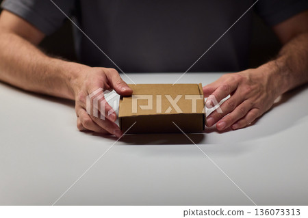 Person unpacks device, Individual reveals compact electronic component inside, Person diligently removes protective cover to access electronic device within home environment 136073313