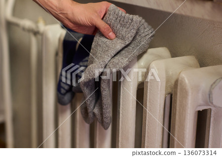 Person placing moist wool socks onto heated radiator fins, Detailed scene of hand carefully positioning damp wool socks on heated metal radiator with knit texture Person placing moist wool socks onto heated radiator fins, Detailed scene of hand carefully positioning damp wool socks on heated metal radiator with knit texture 136073314