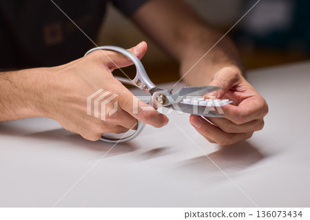 Precise scissors work with blister pack disposal focus, Engaged in cautious scissors cutting of blister pack on clean countertop emphasizing safety and responsible disposal 136073434