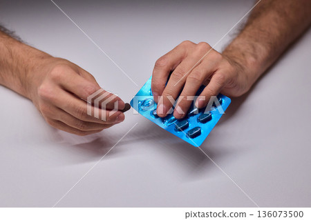 Hands extracting capsule from blister pack gently, closeup on fingertips and foil on white tabletop, quiet moment of dosing accuracy and calm preparation for intake Hands extracting capsule from blister pack gently, closeup on fingertips and foil on white tabletop, quiet moment of dosing accuracy and calm preparation for intake 136073500