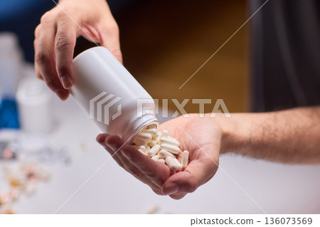 Closeup of caregiver preparing medication in warm bathroom environment, Wrist and fingers shown as caregiver arranges pills from bottle for daily dosage in soothing lighting Closeup of caregiver preparing medication in warm bathroom environment, Wrist and fingers shown as caregiver arranges pills from bottle for daily dosage in soothing lighting 136073569