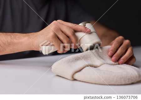 Close view of lint tool on wool, Man using lint roller to clean wool hat texture, Detailed scene of hand grooming fuzz from soft knitted wool hat with lint roller Close view of lint tool on wool, Man using lint roller to clean wool hat texture, Detailed scene of hand grooming fuzz from soft knitted wool hat with lint roller 136073706