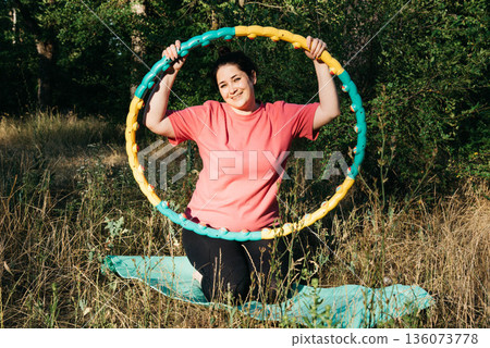 A plus-size woman is doing gymnastics in nature. A woman with a hoop in her hands. Outdoor sports. A plus-size woman is doing gymnastics in nature. A woman with a hoop in her hands. Outdoor sports. 136073778