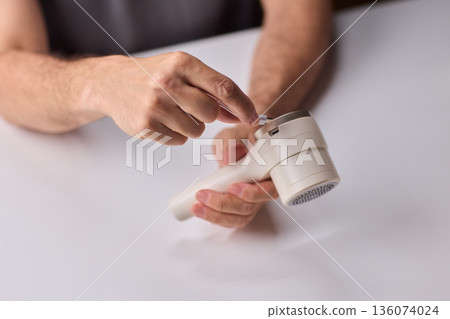Close view of lint tool on wool, Man using lint roller to clean wool hat texture, Detailed scene of hand grooming fuzz from soft knitted wool hat with lint roller Close view of lint tool on wool, Man using lint roller to clean wool hat texture, Detailed scene of hand grooming fuzz from soft knitted wool hat with lint roller 136074024