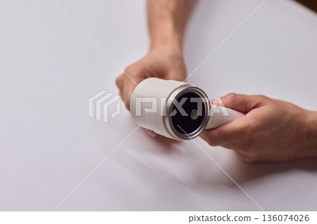 Close view of lint tool on wool, Man using lint roller to clean wool hat texture, Detailed scene of hand grooming fuzz from soft knitted wool hat with lint roller 136074026