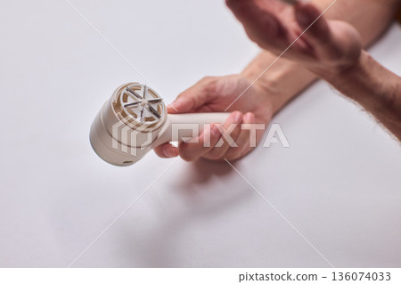 Close view of lint tool on wool, Man using lint roller to clean wool hat texture, Detailed scene of hand grooming fuzz from soft knitted wool hat with lint roller 136074033
