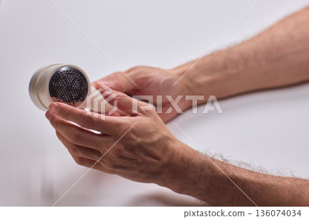 Close view of lint tool on wool, Man using lint roller to clean wool hat texture, Detailed scene of hand grooming fuzz from soft knitted wool hat with lint roller 136074034
