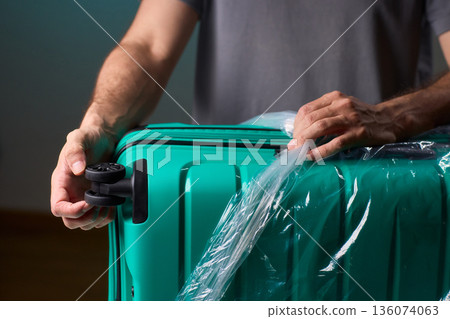 Luggage wrapping process, Worker securing suitcase with protective plastic film, Ensuring safety and protection through meticulous wrapping of belongings for travel Luggage wrapping process, Worker securing suitcase with protective plastic film, Ensuring safety and protection through meticulous wrapping of belongings for travel 136074063