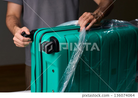 Luggage wrapping process, Worker securing suitcase with protective plastic film, Ensuring safety and protection through meticulous wrapping of belongings for travel Luggage wrapping process, Worker securing suitcase with protective plastic film, Ensuring safety and protection through meticulous wrapping of belongings for travel 136074064