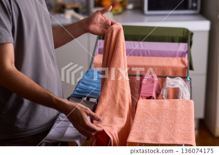 Housekeeper hangs pink towel in bathroom, Bright bathroom scene with towels drying after laundry, Indoor routine where housekeeper air dries linens on metal rack in sunlight 136074175