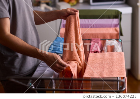 Housekeeper hangs pink towel in bathroom, Bright bathroom scene with towels drying after laundry, Indoor routine where housekeeper air dries linens on metal rack in sunlight 136074225