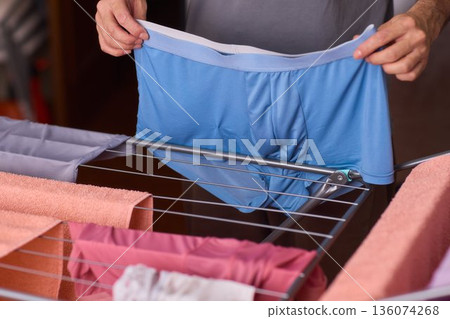 Home interior scene with clothing being gently organized and dried, Domestic chore involving male hands carefully placing cotton underwear on mesh sorter in apartment Home interior scene with clothing being gently organized and dried, Domestic chore involving male hands carefully placing cotton underwear on mesh sorter in apartment 136074268