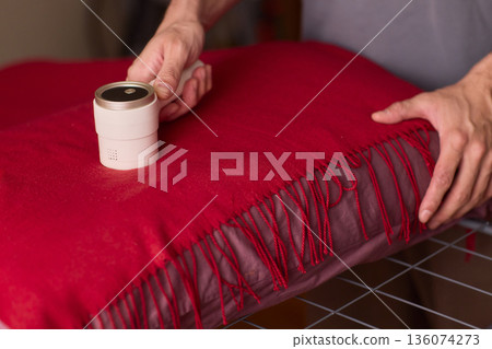 Hands cleaning red wool scarf with lint roller across fringed fabric, closeup texture, warm bedroom lighting, careful motion, pet hair removal, garment ready for outing Hands cleaning red wool scarf with lint roller across fringed fabric, closeup texture, warm bedroom lighting, careful motion, pet hair removal, garment ready for outing 136074273